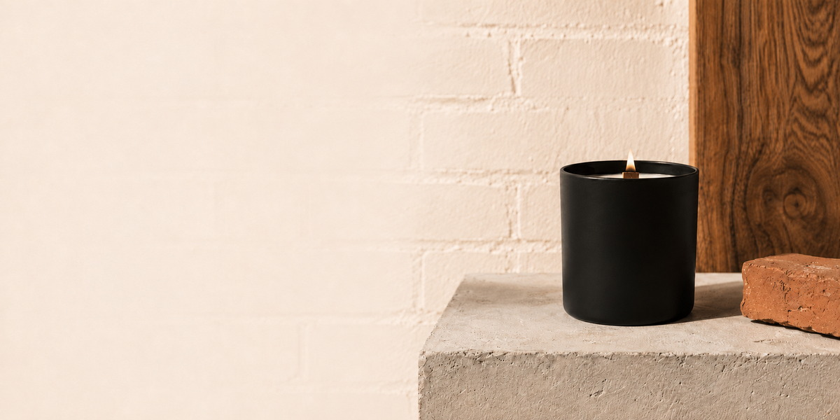 Bougie noire à mèche de bois dans un décor de brique, béton et bois